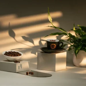 Chávena de café Gold Cuvee no topo de um mostrador e ao lado grãos de café e uma planta